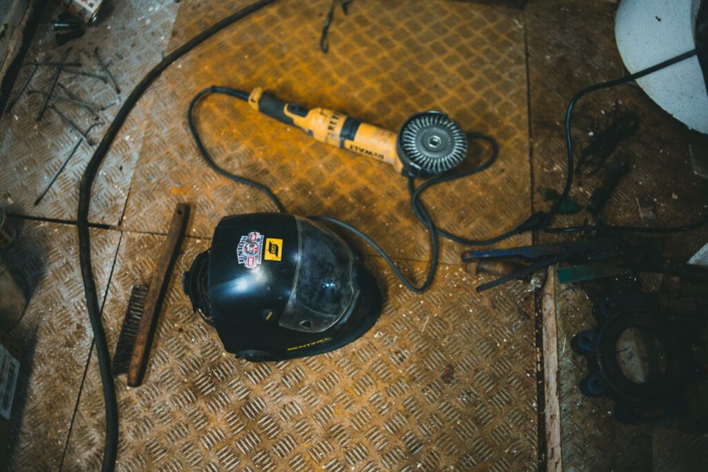 Overhead view of a workshop scene with an angle grinder and welding helmet on a textured floor.