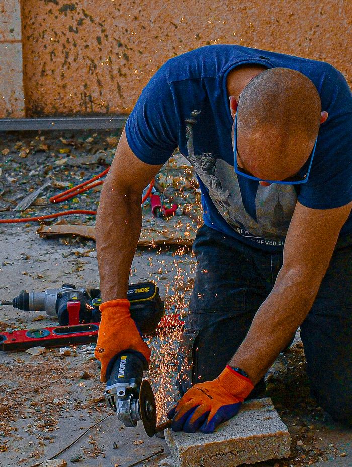 A man using an angle grinder, creating sparks as he works on a construction site.