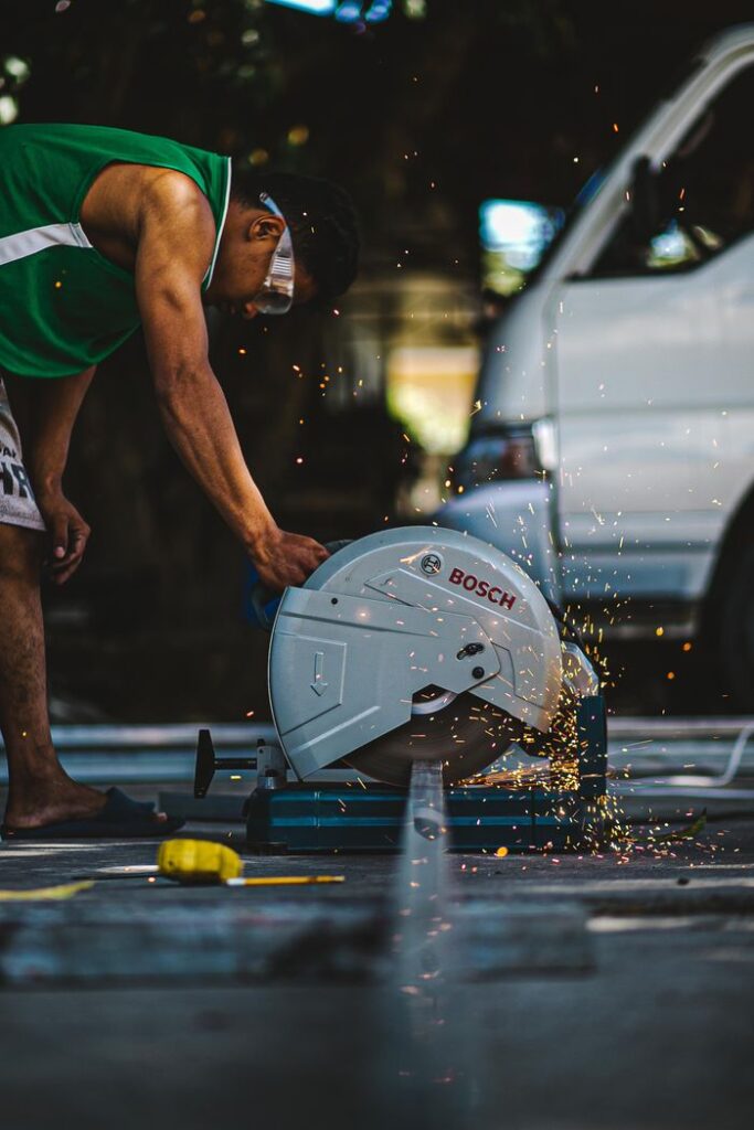 A focused industrial worker using a metal cutting saw outdoors, creating sparks during the process.