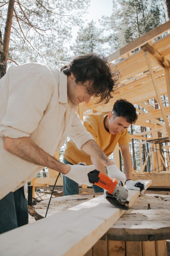 Two men working with power tools on an outdoor carpentry construction site.